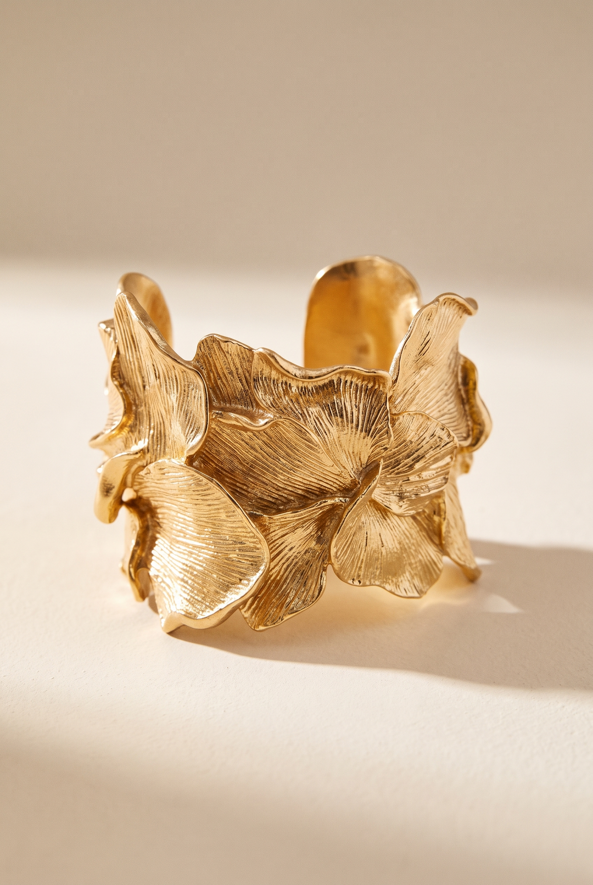 Gold metallic textured flowers cuff bracelet on a warm cream surface